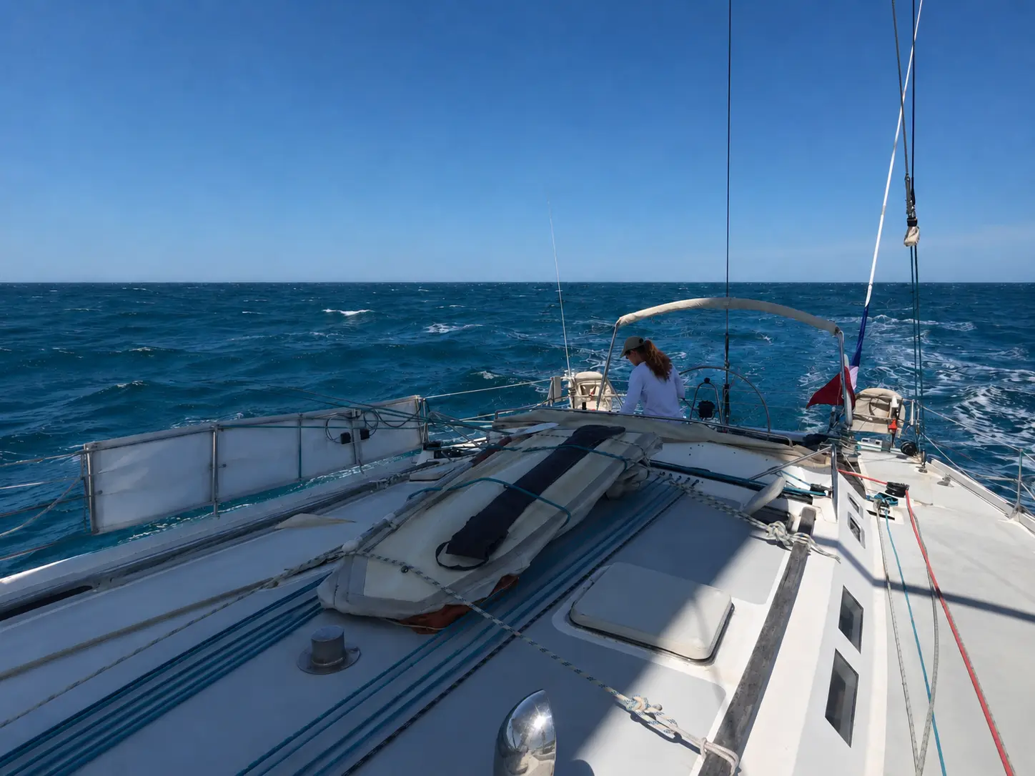ZORYA foredeck view underway offshore with helmsman at the wheel and French ensign flying