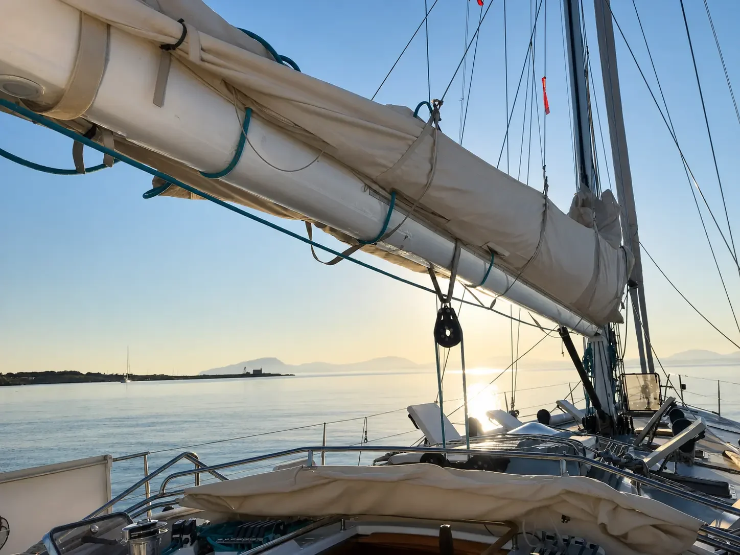 ZORYA boom and stowed mainsail at golden hour, coastline and setting sun astern
