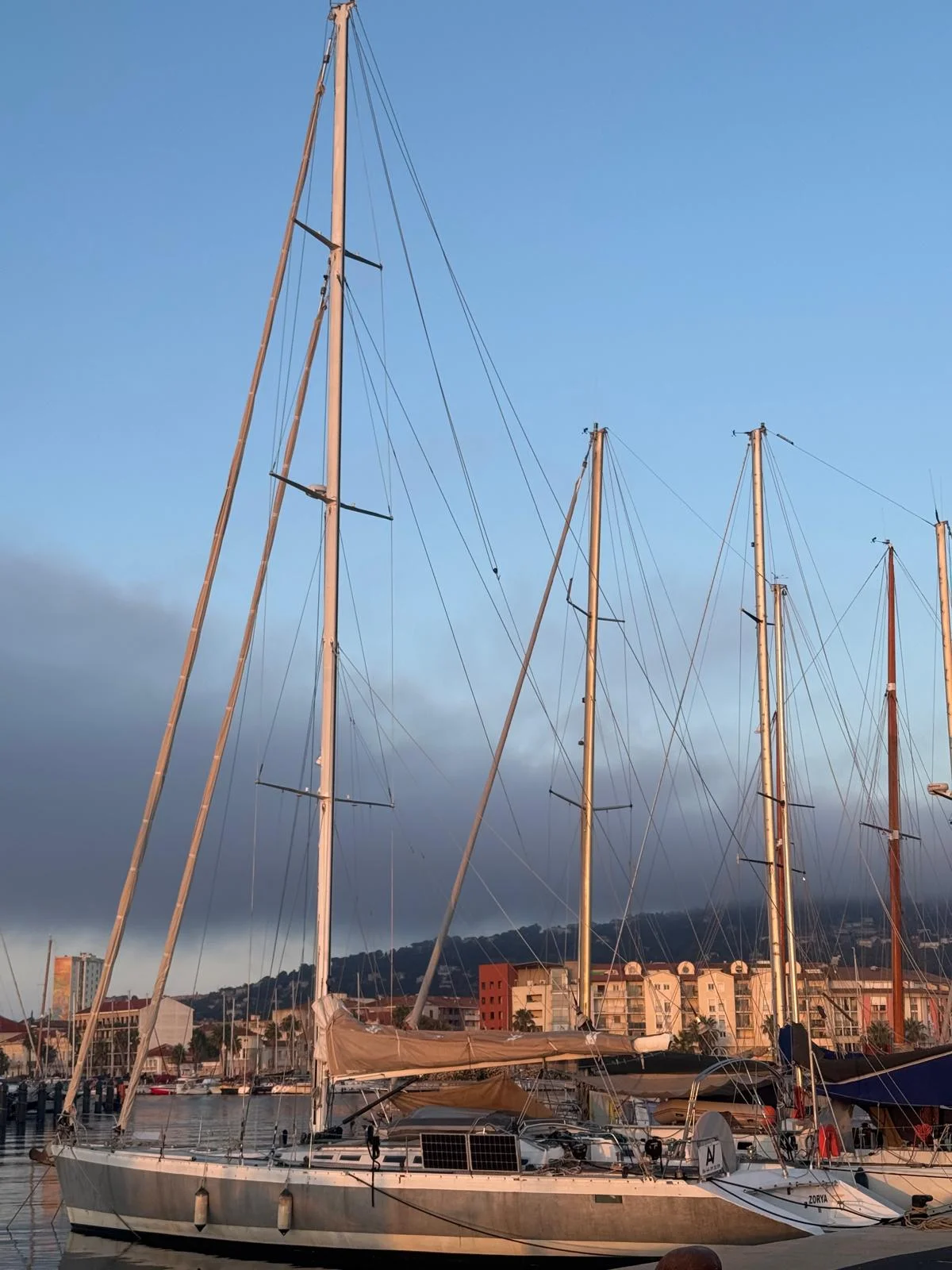ZORYA Levrier 18 berthed in Sète marina at dawn, tall aluminium mast and town behind